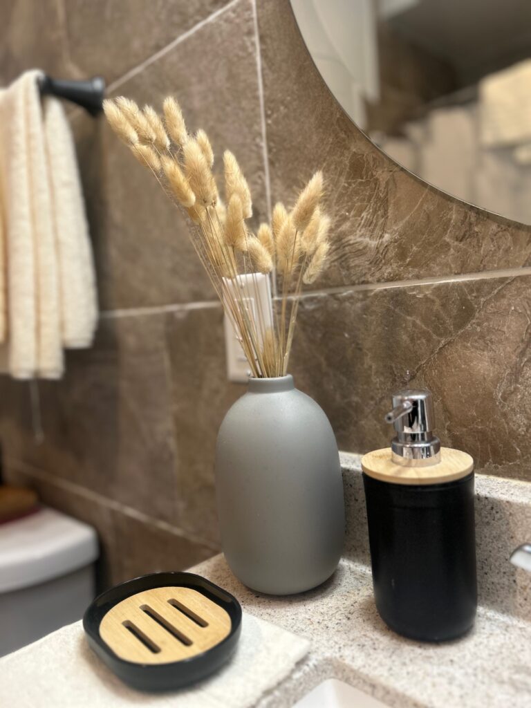 close up of gray vase with pampas grass, black bath accessories: soup dish and liquid soap dispenser.