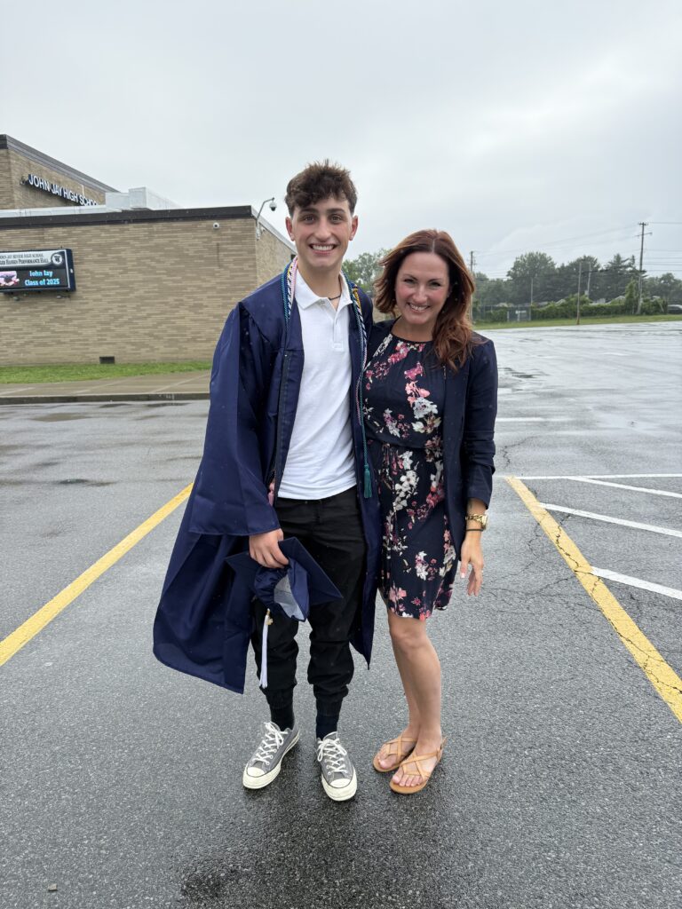 Mother and son, with son in graduation gown, standing in school parking lot