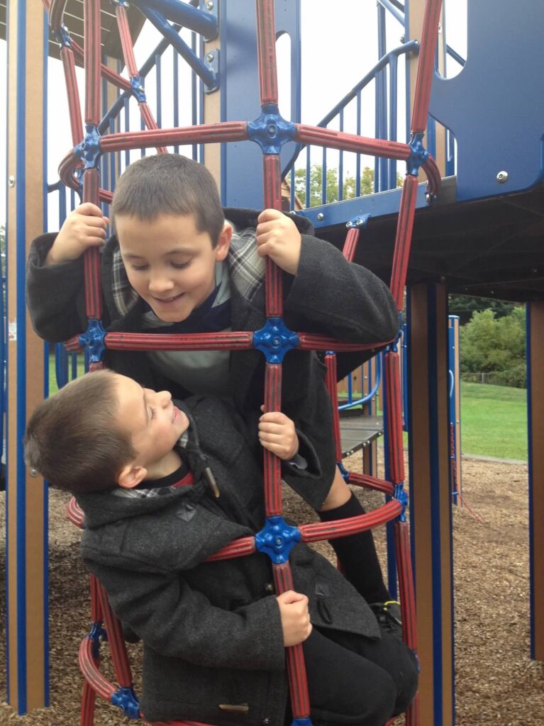 school age boys in winter jackets playing on climbing gym at playground
