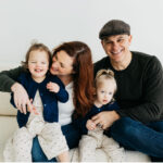 Family photo with white backdrop, featuring mother, father and twin girls