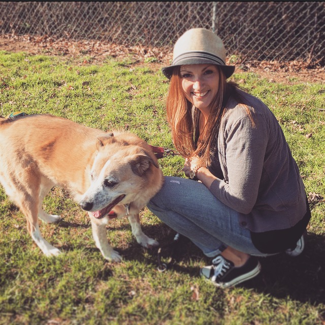 Woman kneeling next to a dog, smiling back at the camera