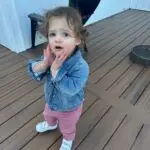 Curly haired brunette toddler with hands to her cheeks in an “oh no” expression