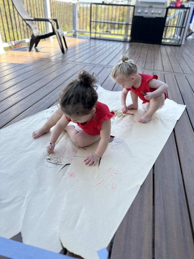 toddler girls outside on deck, coloring on oversized paper roll