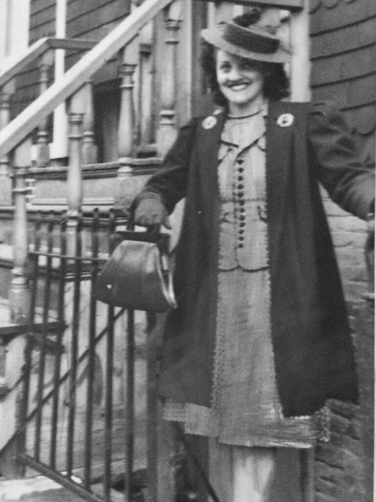 vintage photo 1950's woman in dress, coat, hat, holding bag, wearing heels and smiling on the steps of a brownstone in Brooklyn