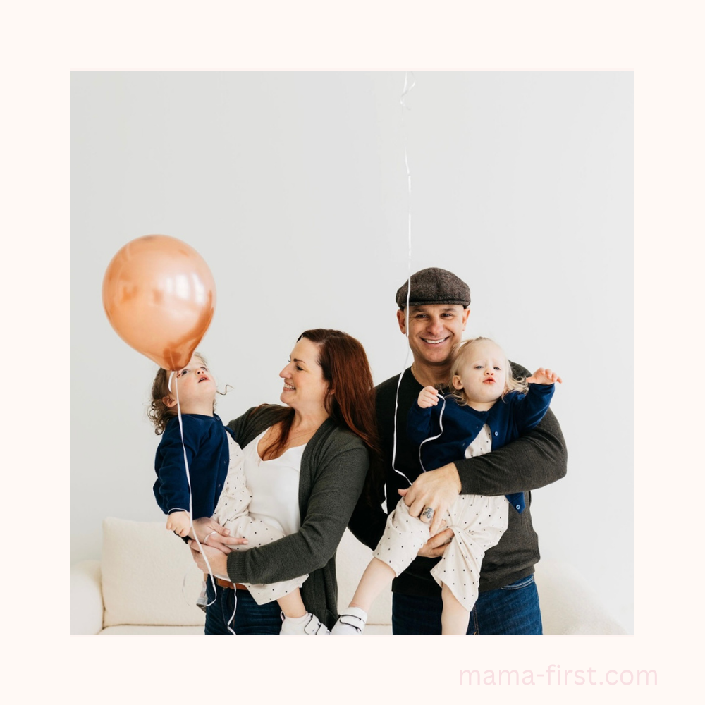 Family home pic with mom, dad twin girls being held by each parent and pink balloon