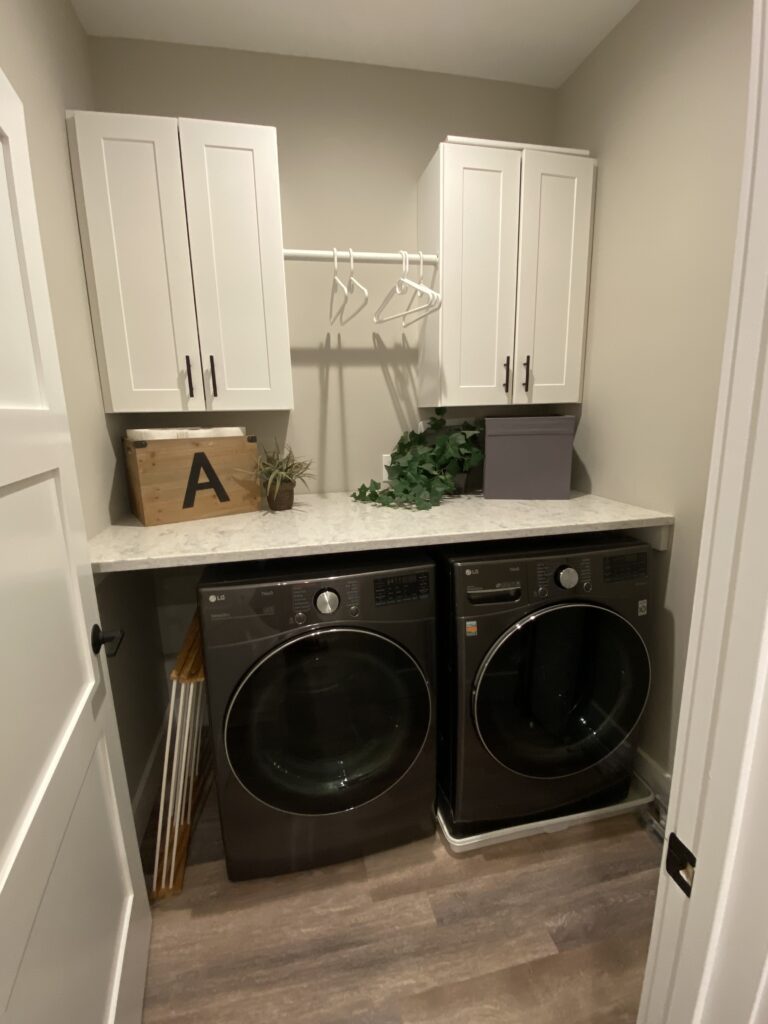 Clean but boring laundry room with light countertops, white upper cabinets and clothes hanger between