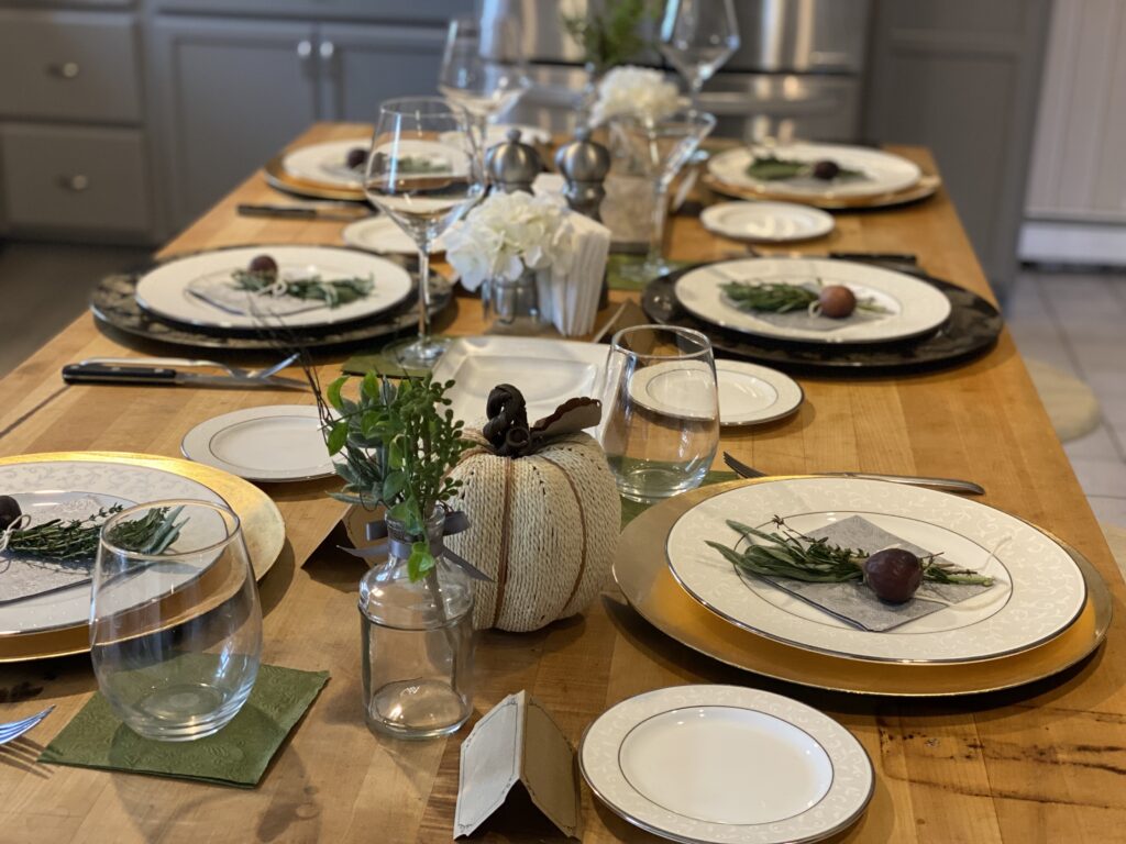 butcher block table set with fall decor, gold chargers and white porcelain place settings. burlap and herb sprig on each plate.