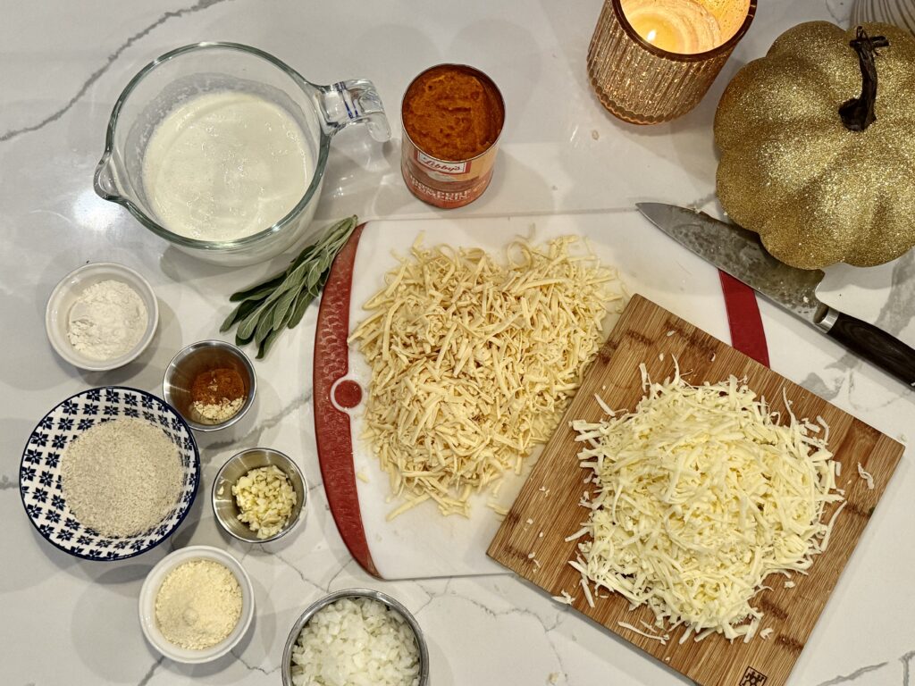 Assembled Mise en Place: milk, flour, sage, spices, breadcrumbs, spices, minced garlic, parmesan, superfine diced onion, fresh shredded fontina, freshly shredded smoked gouda, pumpkin puree… chef's knife, gold pumpkin and gold candle styling the pic.