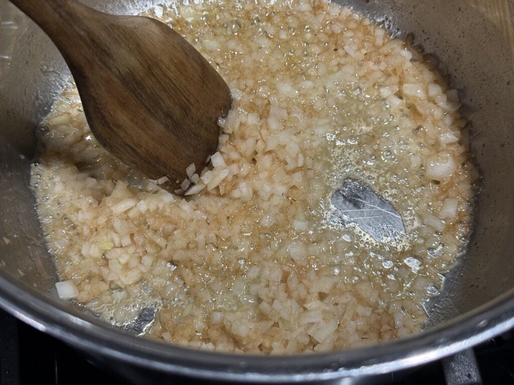cooked onions with flour and spices in stainless steel pot being mixed with wooden spoon
