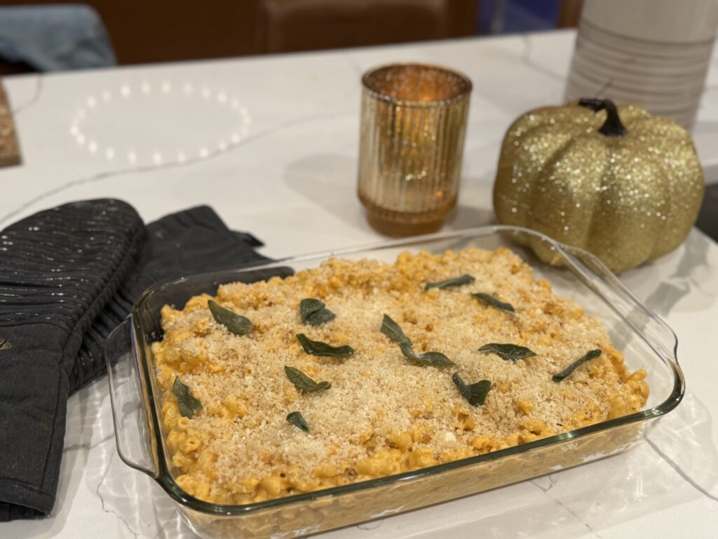 glass tray of pumpkin macaroni and cheese with fried sage and panko topping styled on white quartz counter with gold Thanksgiving holiday accents