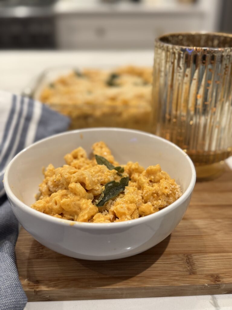 pumpkin Mac & cheese with fried safe and panko topping in white bowl on wooden board, styled with allclad blue & white towel and gold, fluted candle