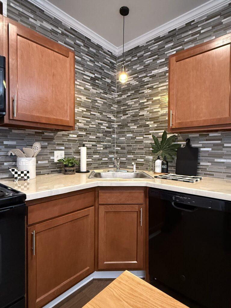 corner of kitchen shot; sink centered, design decor featured (black and whites, plus greenery with plants; buffalo plaid cow and dishtowel)