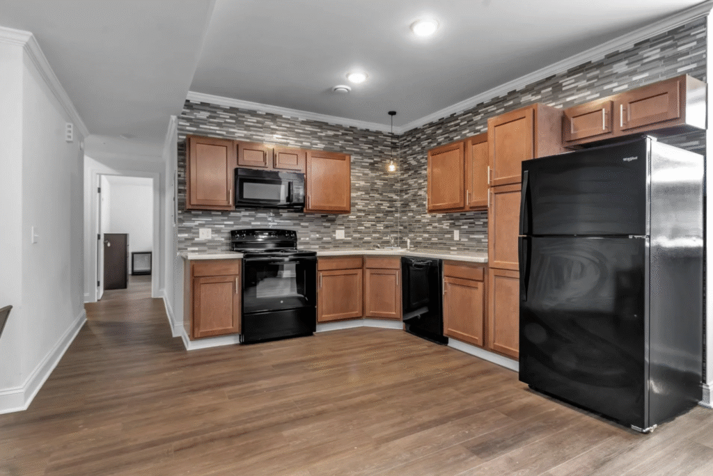 Apartment kitchen with excessive small gray tile backsplash, wood cabinetry and black appliances 