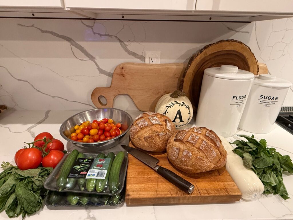 Summer panzanella salad ingredients including tomatoes, basil, cucumbers, sourdough bread, and mozzarella cheese.