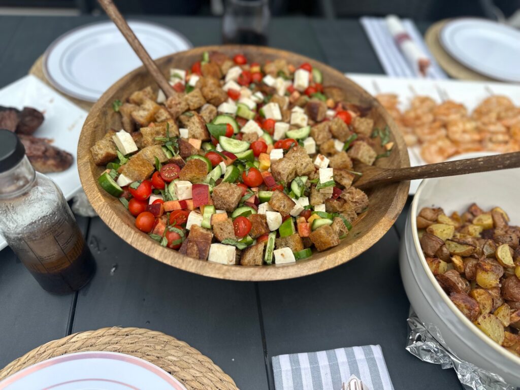 Homemade peach panzanella salad served outdoors in a wooden bowl with toasted sourdough, fresh mozzarella, tomatoes, cucumbers, and basil.