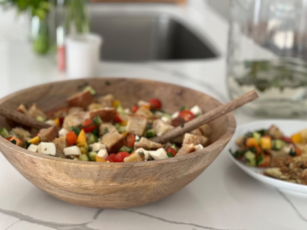 Summer peach panzanella salad with sourdough bread, fresh mozzarella, cucumbers, tomatoes, basil, and peaches in a large wooden serving bowl.