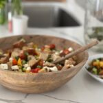Summer peach panzanella salad with sourdough bread, fresh mozzarella, cucumbers, tomatoes, basil, and peaches in a large wooden serving bowl.