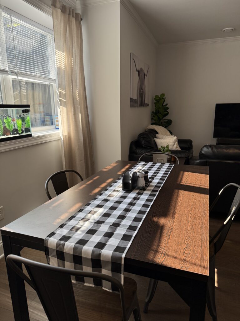 Wooden dining/breakfast table with black and white buffalo plaid table runner and black and white salt and pepper shakers, in morning light