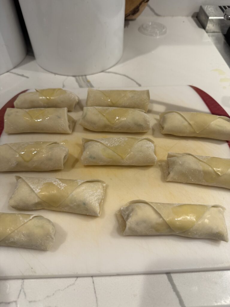 uncooked egg rolls, filled, rolled, and sealed, in rows on a cutting/prep board, ready to be fried.