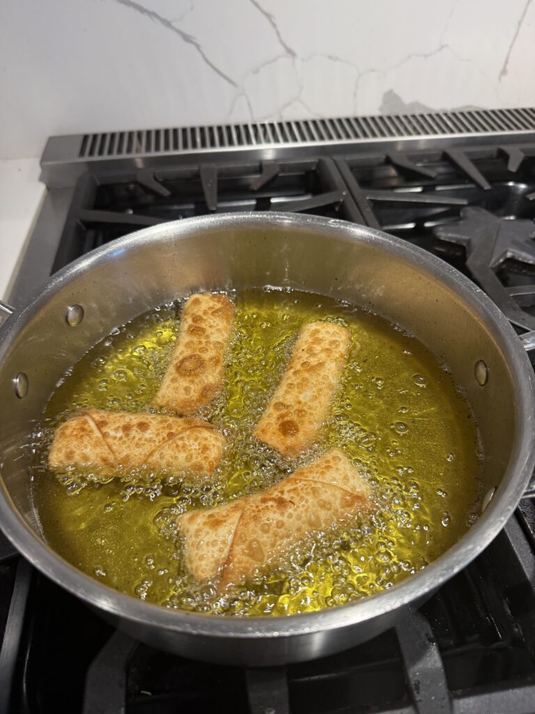 crab egg rolls with crispy wrapper being fried in stainless steel pot on stovetop
