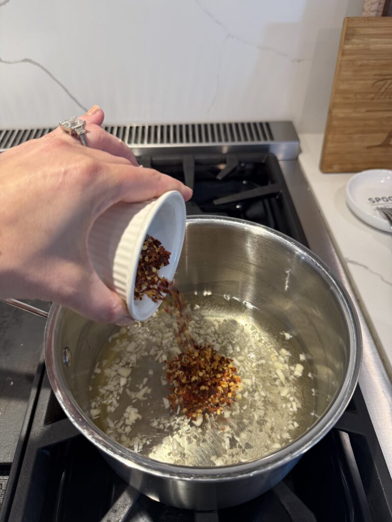red chili flakes being poured into pot already simmering with dissolved sugar in water and rice wine vinegar.  