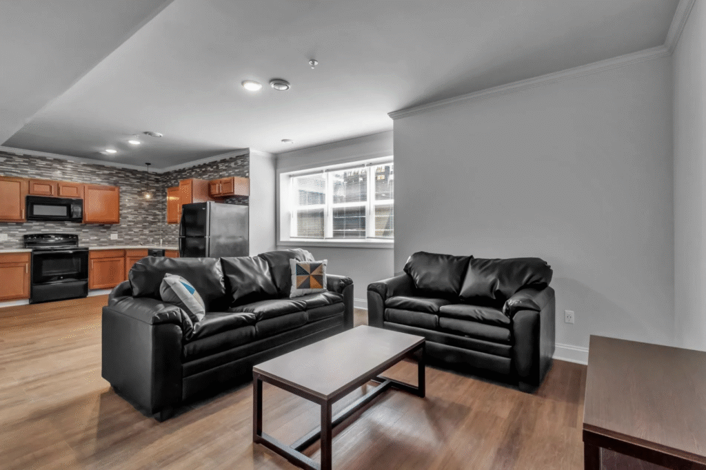 Before shot of the apartment living room. two black leather couches sitting at a 90 degree angle to one another, coffee table, no rug or decor